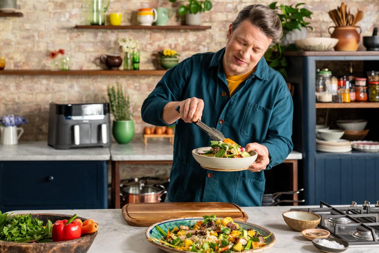 Dish Gnarly Pork & Pineapple Noodles Pictured: Jamie Oliver plating up food - tongs in one hand, bowl in the other.