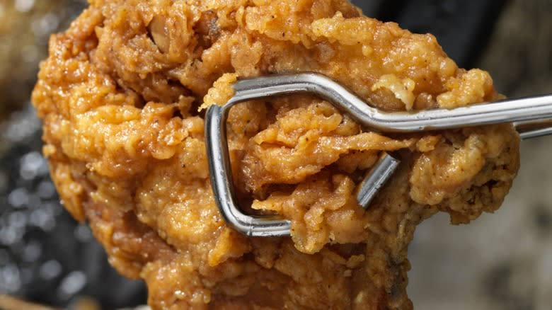 Closeup of tongs holding a piece of fried chicken