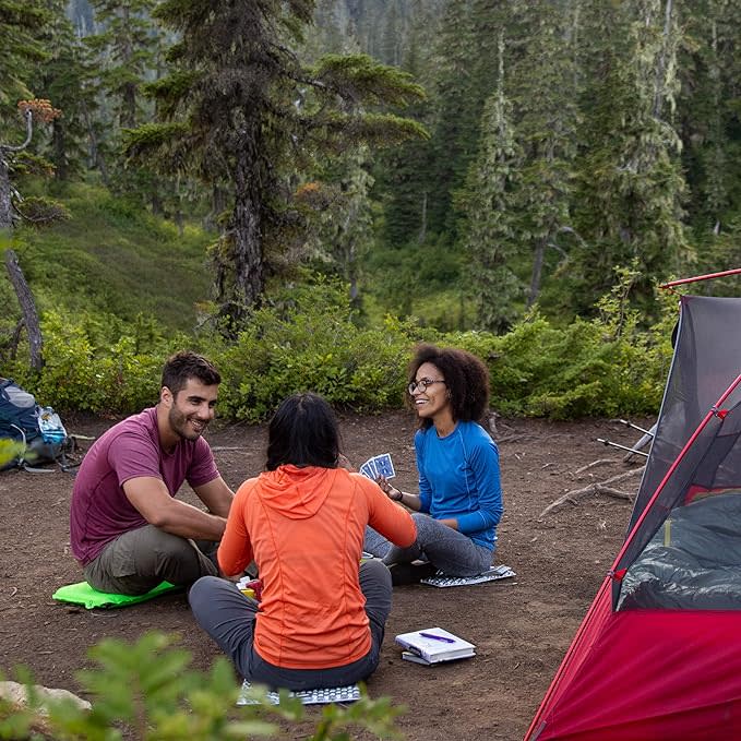 Three people sit on their own Therm-a-Rest Z seats in a circle on the ground at a campsite