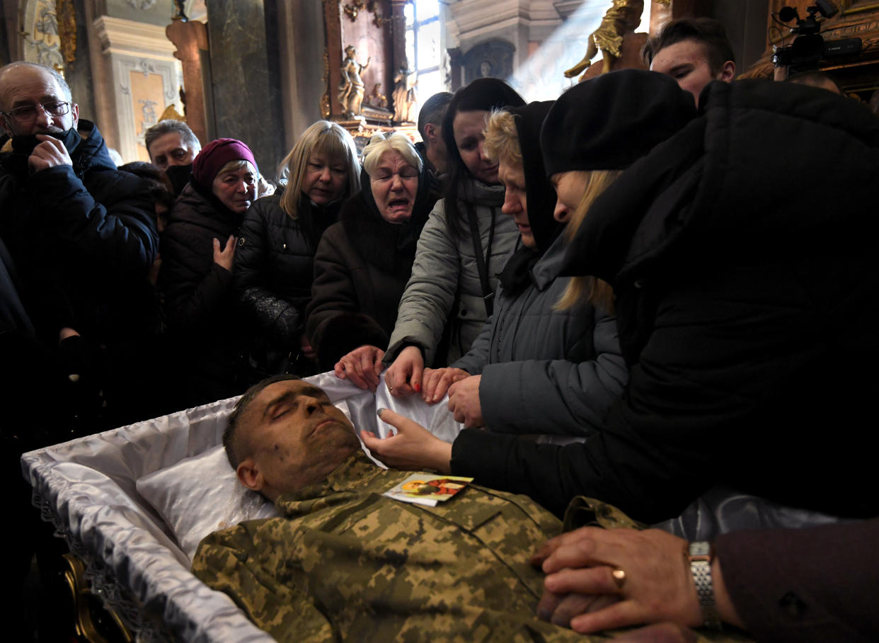 Crying mourners stand around the casket of a fallen soldier.