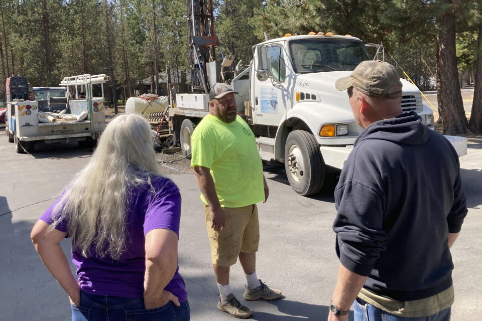 FiLE - Linda Jincks and her husband Rodger talk with driller Shane Harris as his crew drills a new well for the Jincks at their home in La Pine, Ore., on Aug. 26, 2021. Oregon has long been known as a mecca for high-quality marijuana, but that reputation has come with a downside: illegal growers who offer huge amounts of cash to lease or buy land and then leave behind pollution, garbage and a drained water table. (AP Photo/Andrew Selsky, File)