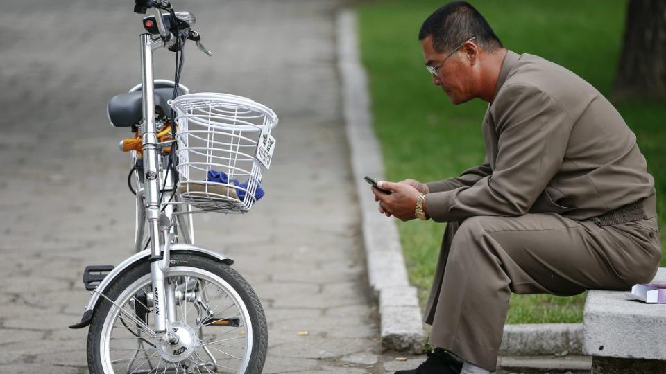 A man uses his mobile phone next to an electric bicycle in downtown Pyongyang.