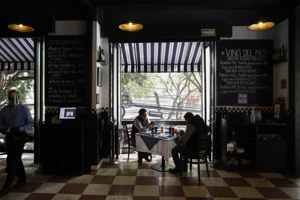 Diners sit at a table in front of open doors on the second story of Argentine grill Quebracho, in the Cuauhtemoc neighborhood of Mexico City, Monday, Jan. 11, 2021. More than three weeks into Mexico City's second pandemic shutdown some restaurateurs worried about their ability to survive ignored official warnings and opened limited seating Monday under the slogan, "Abrir o Morir," Spanish for "Open or Die." (AP Photo/Rebecca Blackwell)