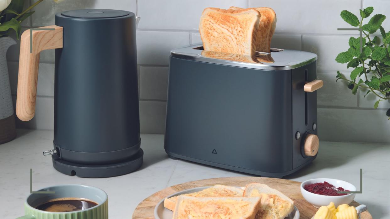  Kitchen countertop with matt grey Aldi kettle with wooden handle and matching toaster beside a wooden plate with toast to show the new Aldi kitchen appliances in stores. 