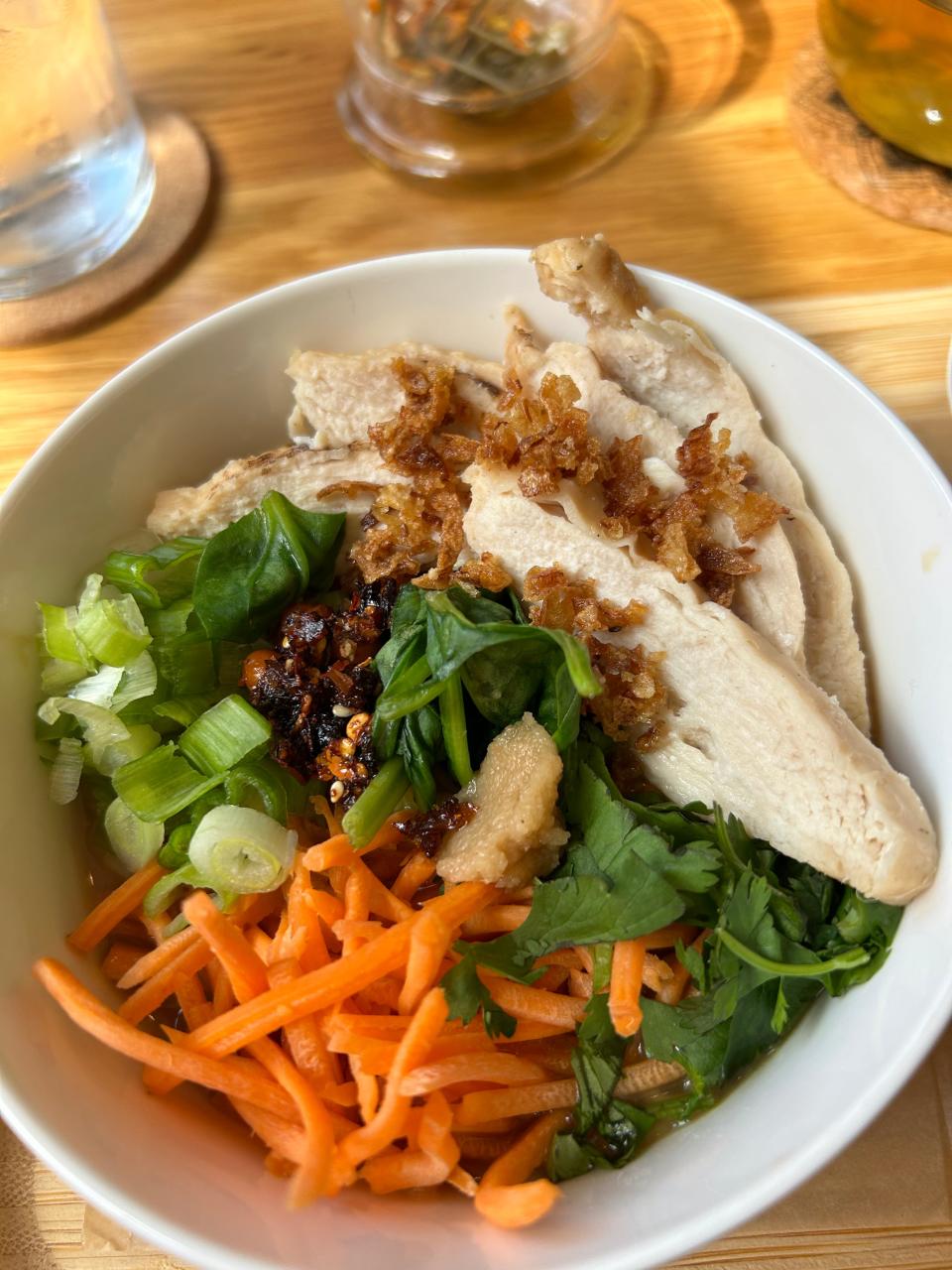 Ramen with grilled chicken is topped with scallions, shredded carrots, cilantro, crispy onions, garlic and crushed chili flakes in olive oil at SRINA.
