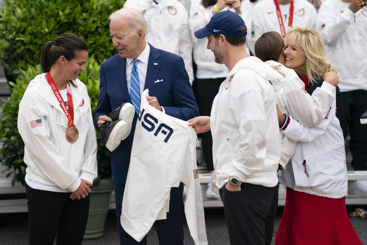 President Joe Biden is presented with Team USA gear during an event with the Tokyo 2020 Summer Olympic and Paralympic Games, and Beijing 2022 Winter Olympic and Paralympic Games, on the South Lawn of the White House, Wednesday, May 4, 2022, in Washington. From left, speed skater Brittany Bowe, Biden, curler John Shuster, Paralympic triathlete Melissa Stockwell, and first lady Jill Biden. (AP Photo/Evan Vucci)