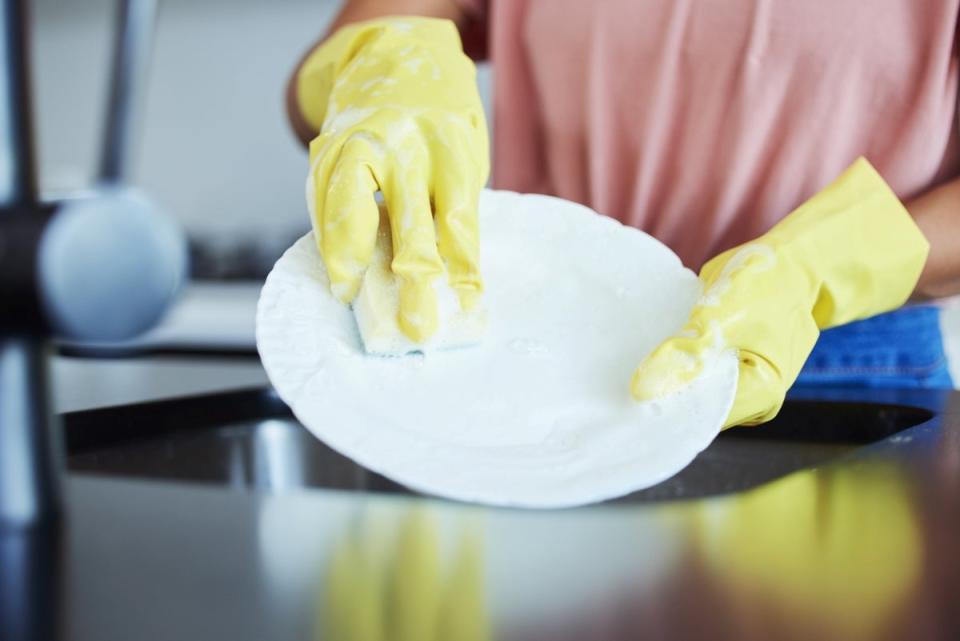 Person wearing yellow rubber gloves using a sponge to clean a dish.