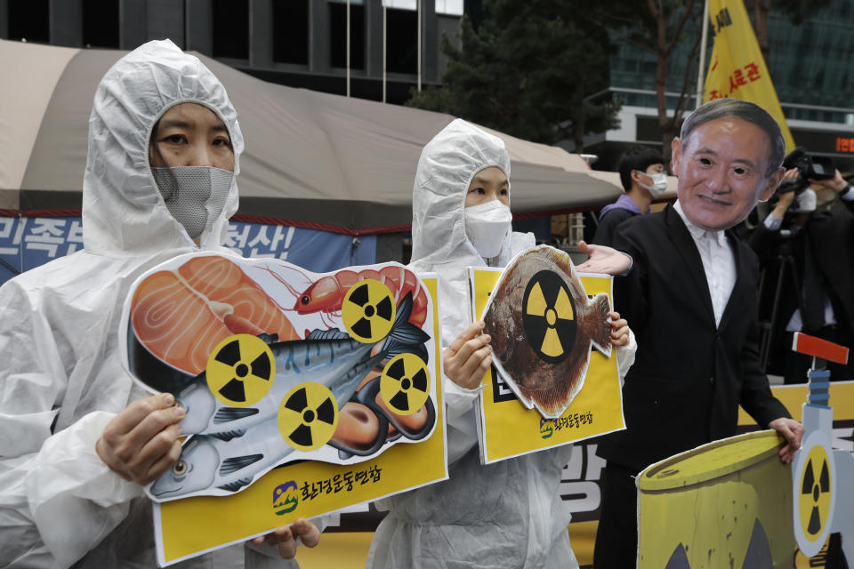 FILE - In this April 13, 2021, file photo, environmental activists wearing a mask of Japanese Prime Minister Yoshihide Suga and protective suits perform to denounce the Japanese government's decision to release treated radioactive Fukushima water, near the Japanese Embassy in Seoul, South Korea. Japan’s government adopted an interim plan Tuesday, Aug. 24, 2021 that it hopes will win support from fishermen and other concerned groups for a planned release into the sea of treated but still radioactive water from the wrecked Fukushima nuclear plant. (AP Photo/Lee Jin-man, FIle)