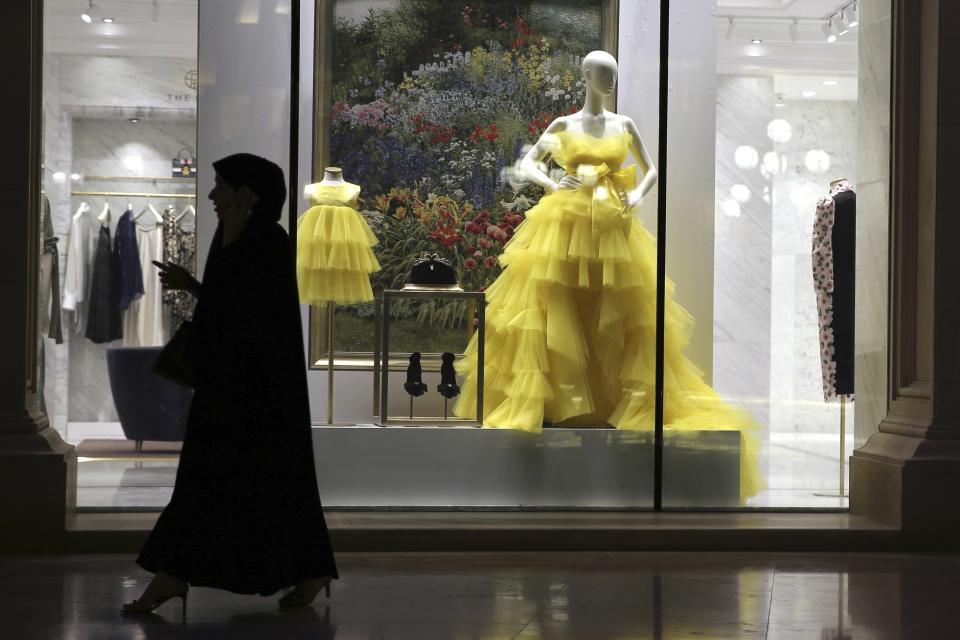 FILE - A woman passes by fashion outfit at the Al Hazm luxury mall, in Doha, Qatar, Wednesday, April 24, 2019. The foreign fans descending on Doha for the 2022 FIFA World Cup will find a country where women work, hold public office and cruise in their supercars along the city's palm-lined corniche. (AP Photo/Kamran Jebreili, File)