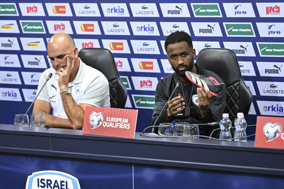 Israel team captain Eli Dasa, right, sits by head coach Alon Hazan as he shows a shoe of a kidnapped Israeli boy during a press conference, before a training session for the Euro 2024 group I qualifying soccer match between Israel and Switzerland at the Pancho Arena in Felcsút, Hungary, Tuesday, Nov. 14, 2023. The captain of Israel's soccer team on Tuesday displayed the shoe of a young boy that he said was kidnapped by Hamas militants during their deadly Oct. 7 raid, an act of solidarity with those Israelis still being held captive in the Gaza Strip ahead of the team's Wednesday game in Hungary. (AP Photo/Denes Erdos)