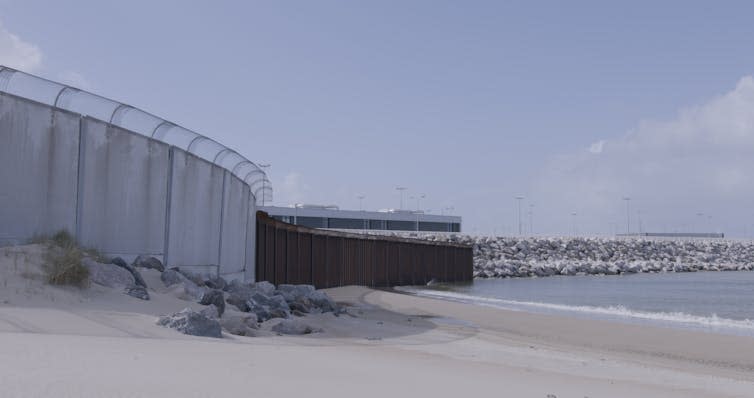 Barbed wire fencing surrounding coastal refugee camp.