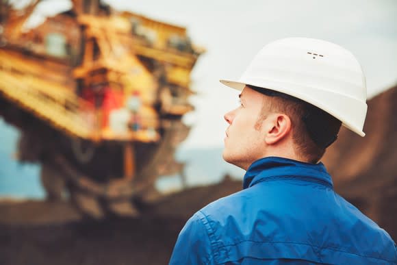 A man wearing a hard hat and looking up at mining equipment