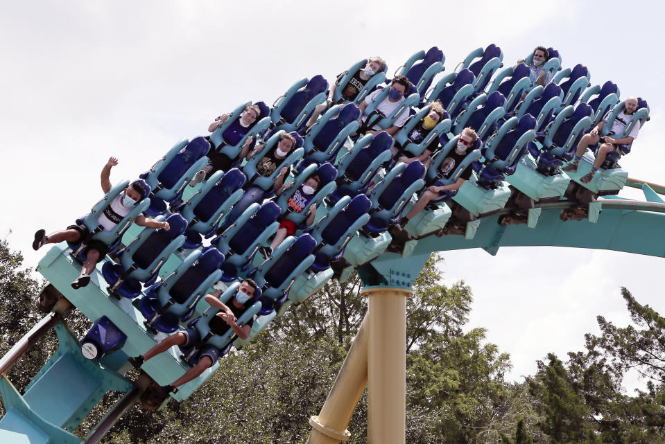 Guests wearing face masks ride a roller coaster at SeaWorld as it reopened with new safety measures in place, Thursday, June 11, 2020, in Orlando, Fla. The park had been closed since mid-March to stop the spread of the new coronavirus. (AP Photo/John Raoux)