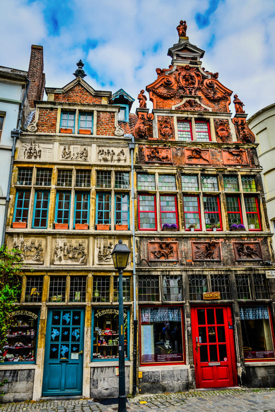 Historic European building with ornate facade, red and blue doors, and a vintage lamp post in front