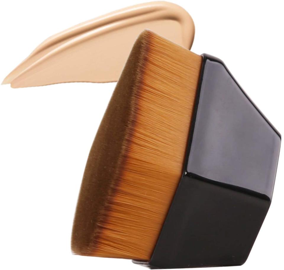 A Daubigny Foundation Makeup Brush with tan bristles and dark brown geometric base is shown next to streaks of beige foundation on a white background