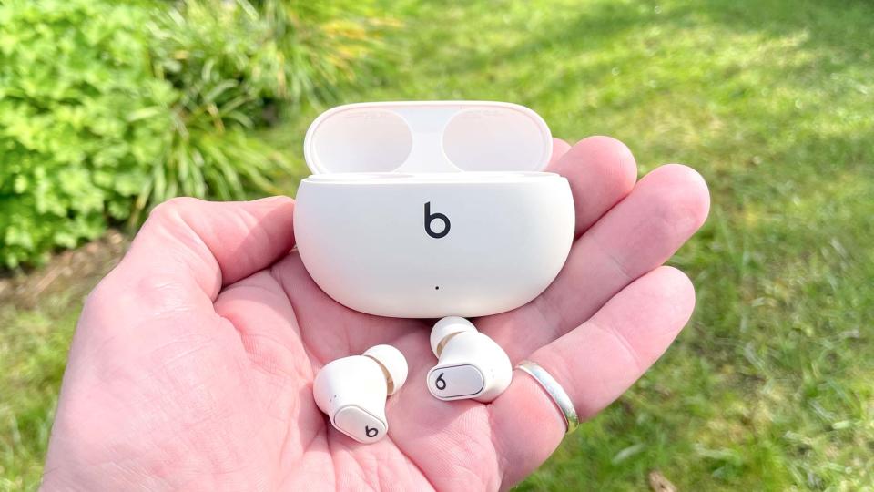 Beats Studio Buds+ held in hand with open charging case outdoors