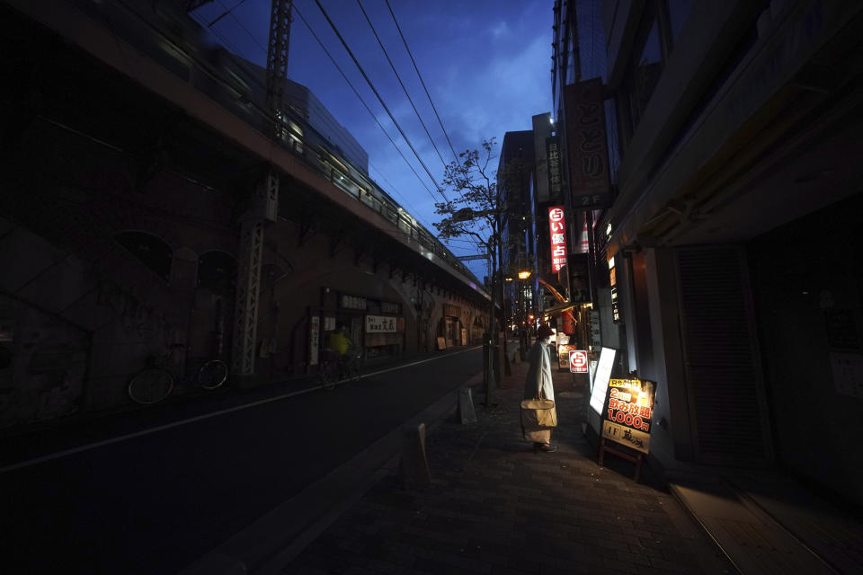 FILE - In this April 28, 2020, file photo, a woman wearing a face mask against the spread of the new coronavirus looks at menu of a restaurant at an empty street in Tokyo. Under Japan's coronavirus state of emergency, people have been asked to stay home. Many are not. Some still have to commute to their jobs despite risks of infection, while others are dining out, picnicking in parks and crowding into grocery stores with scant regard for social distancing. (AP Photo/Eugene Hoshiko, File)