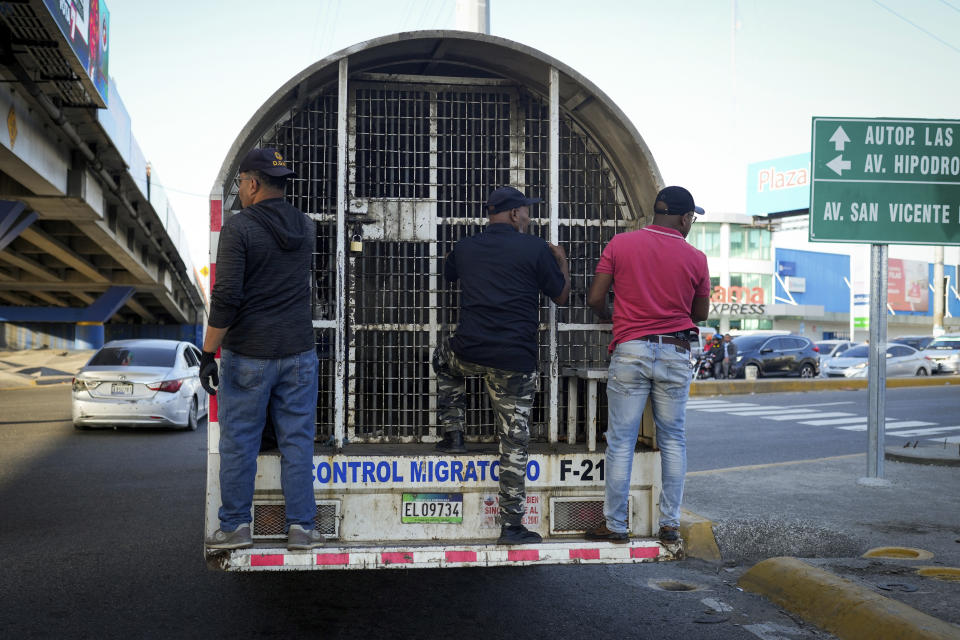 Migration officials stand on the tailgate step of a paddy wagon as they transport undocumented Haitians in Santo Domingo, Dominican Republic, Thursday, May 16, 2024. As soaring violence and political turmoil grip neighboring Haiti, Dominican Republic’s election on May 19 has been defined by calls for more migratory crackdowns and finishing a border wall dividing the countries. (AP Photo/Matias Delacroix)