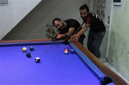 A Free Syrian Army fighter plays pool as his fellow fighter jokes around by aiming his weapon towards the balls as they rest in the old city of Aleppo September 9, 2013. REUTERS/Hamid Khatib