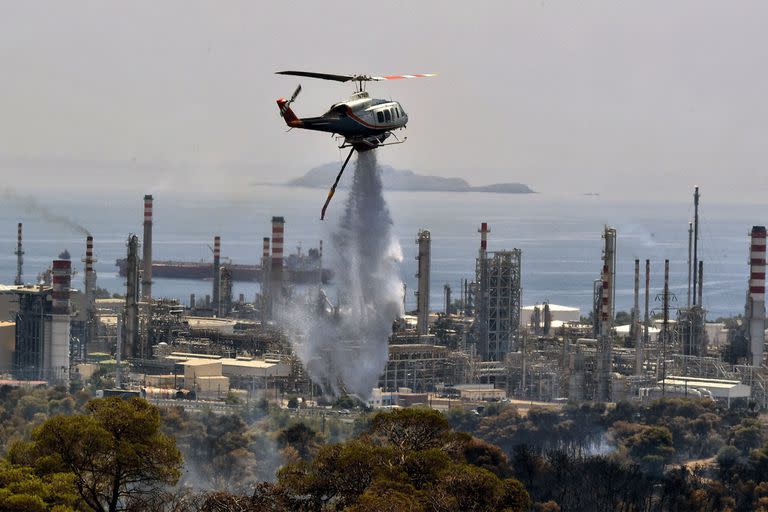 Un helicóptero de extinción de incendios rocía agua durante un incendio forestal cerca de una refinería de petróleo en Agioi Theodoroi, en el oeste de Atenas, el 19 de julio de 2023. (Foto de Valerie GACHE / AFP)