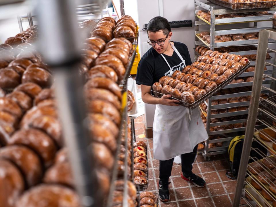 Donut Villa assistant baker Mano looks for space to store freshly made packzi on Tuesday, Feb. 13, 2024, at Donut Villa, a shop that is located in Southwest Detroit and recently reopened following renovations.