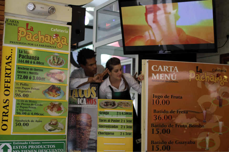 In this June 9, 2012 photo, employees Alexey Piedra, left, and Elizabeth Hernandez stand between menus with photos as they signal customer orders to chefs at the private cafeteria "La Pachanga" in Havana. For decades, Communist-run Cuba has essentially been free of commercial advertising. But it's a knotty problem for thousands of budding entrepreneurs who have embraced President Raul Castro's push for limited free-market reform. So they're turning to guerrilla marketing. (AP Photo/Franklin Reyes)