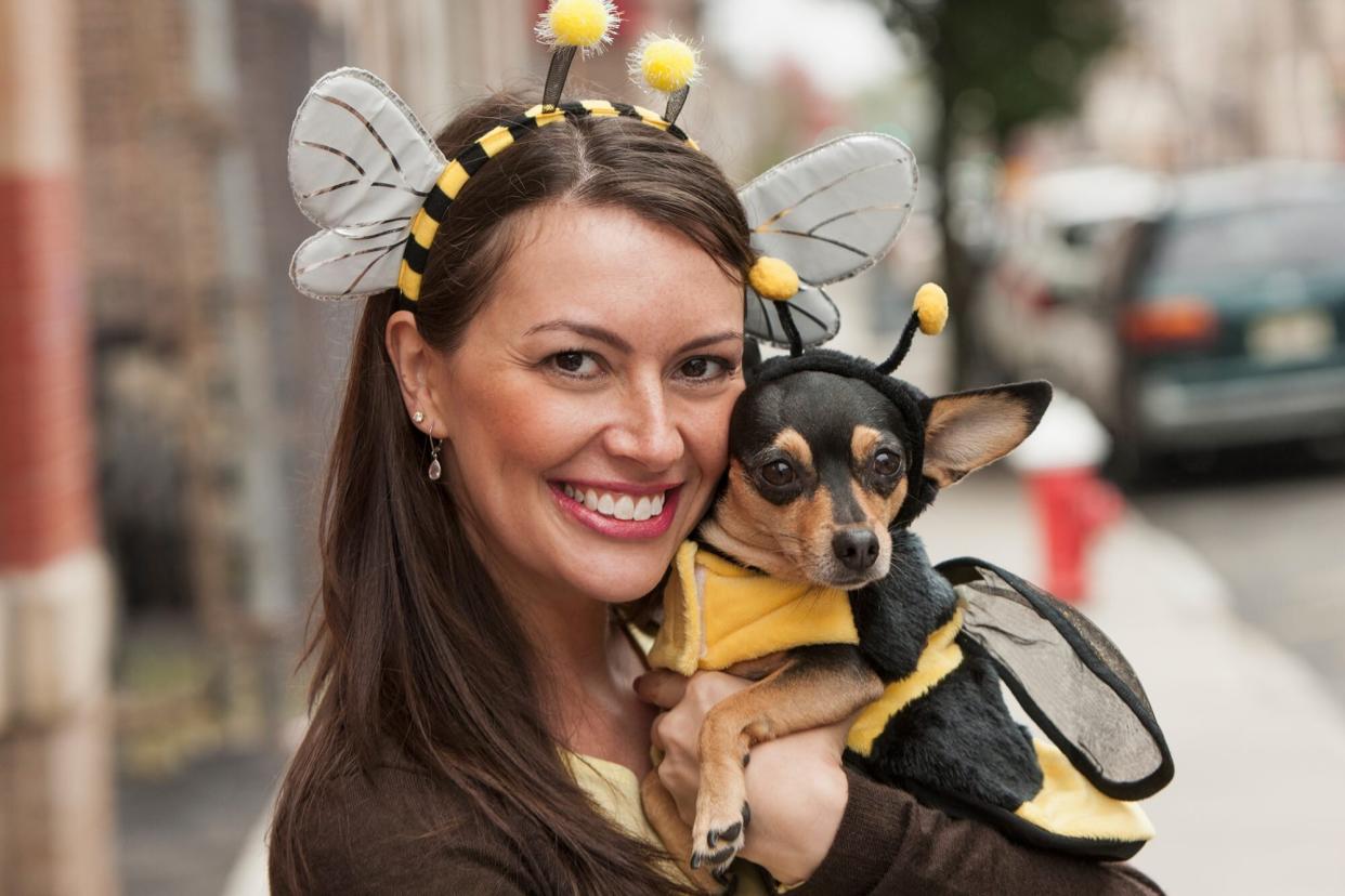 photo of dog in bee halloween costume with a woman wearing a bumblebee headband