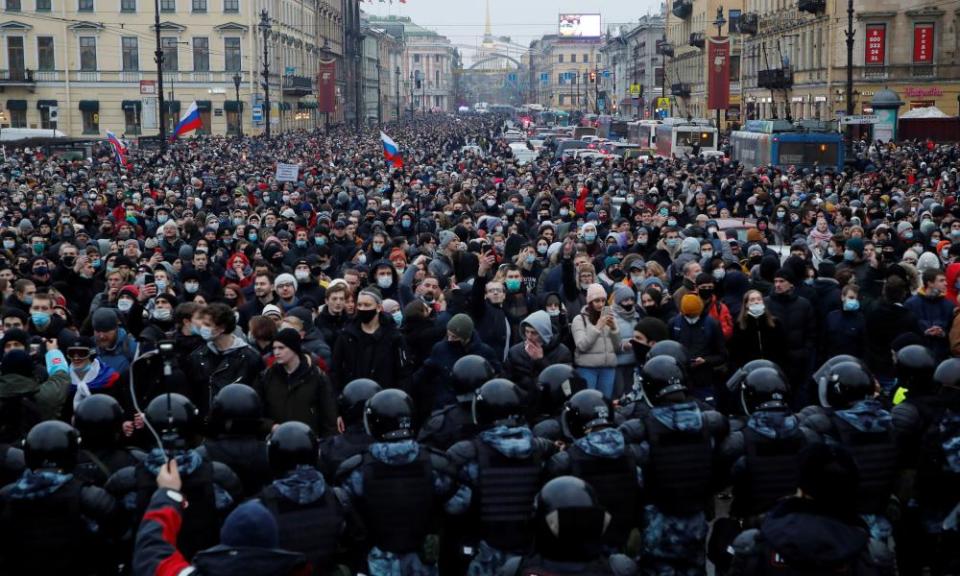 A very large crowd on a St Petersburg street blocked at the end nearest the camera by a large contingent of riot police