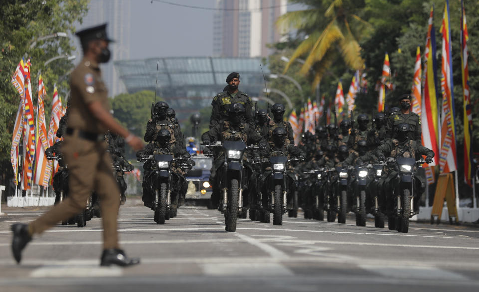 A Sri Lankan police officer walks crosses a road as special force soldiers ride motorbikes during 73rd Independence Day parade rehearsal with a calf elephant in Colombo, Sri Lanka, Wednesday, Feb. 3, 2021. Sri Lanka's independence from British colonial rule is celebrated on Feb. 4 each year. (AP Photo/Eranga Jayawardena)