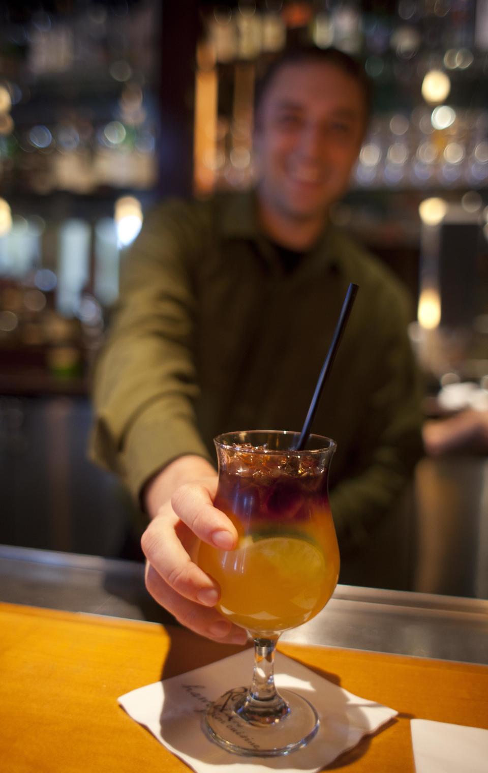 In this photo taken Monday, Aug. 6, 2012, bartender James Smith delivers a $5 Mai Tai during happy hour at the Roy's restaurant in San Francisco. The concept of happy hour when bars offer lower prices or two-for-one specials seems like a widespread tradition, but is actually illegal or restricted in quite a few places. (AP Photo/Eric Risberg)