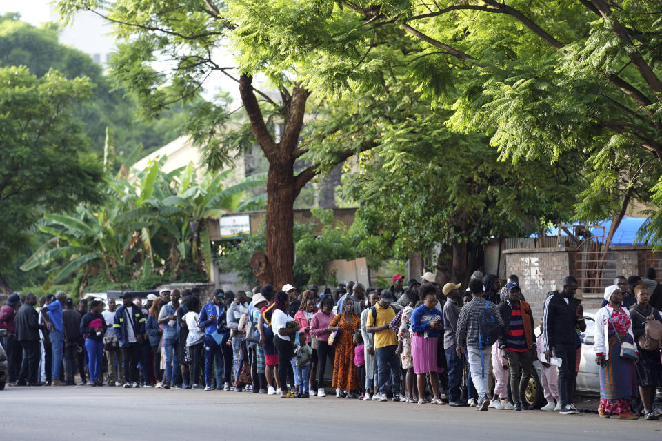 Travelers are seen in a queue outside the passport offices in Harare, Wednesday, Dec. 20, 2023. Atop many Christmas wish lists in economically troubled Zimbabwe is a travel document and people are flooding the passport office this holiday season ahead of a price hike planned in the New Year. The desperation at the office in the capital is palpable as some people fear the hike could push the cost of obtaining a passport out of reach and economic gloom feeds a surge in migration. (AP Photo/Tsvangirayi Mukwazhi)