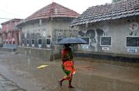 A woman holding an umbrella walks past houses with the walls converted into black boards that children use during their open-air classes at Joba Attpara village