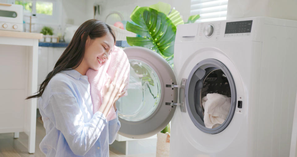 Frau mit frisch gewaschenem Handtuch vor einer Waschmaschine. 