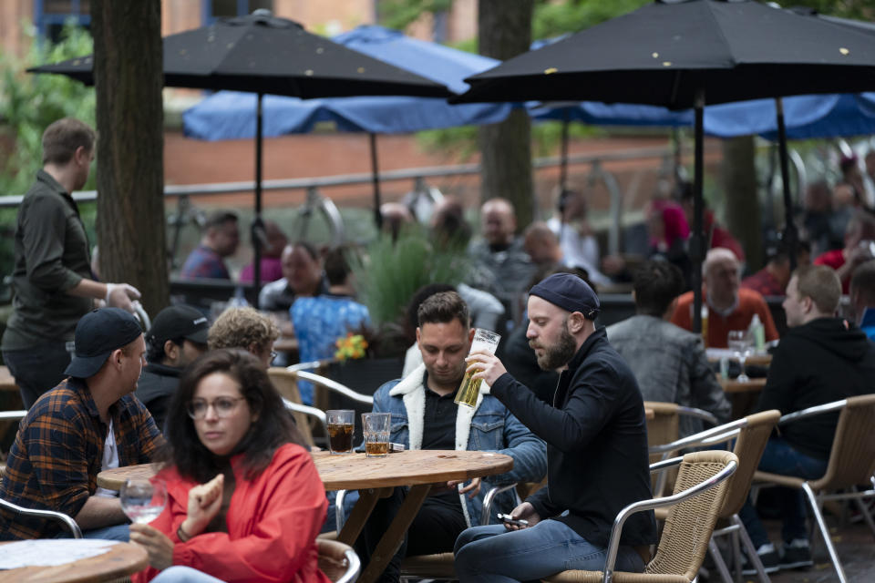 Members of the public are seen at a bar on Canal Street in Manchester's gay village, England, Saturday July 4, 2020. England is embarking on perhaps its biggest lockdown easing yet as pubs and restaurants have the right to reopen for the first time in more than three months. In addition to the reopening of much of the hospitality sector, couples can tie the knot once again, while many of those who have had enough of their lockdown hair can finally get a trim. (AP Photo/Jon Super)