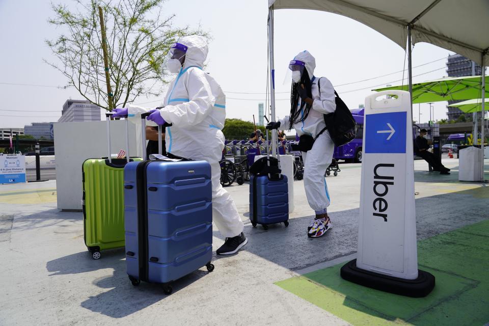 Travelers, Kerri Ann Salomon, left, and a friend arriving from New York City, look for an Uber ride at Los Angeles International Airport's LAX-it pick up terminal Thursday, Aug. 20, 2020. An appeals court has allowed ride-hailing giants Uber and Lyft to continue treating their drivers as independent contractors in California while an appeal works its way through the court. Both companies had threatened to shut down if a ruling went into effect Friday morning that would have forced them to treat all their drivers as employees, a change they said would be impossible to accomplish overnight. (AP Photo/Damian Dovarganes)