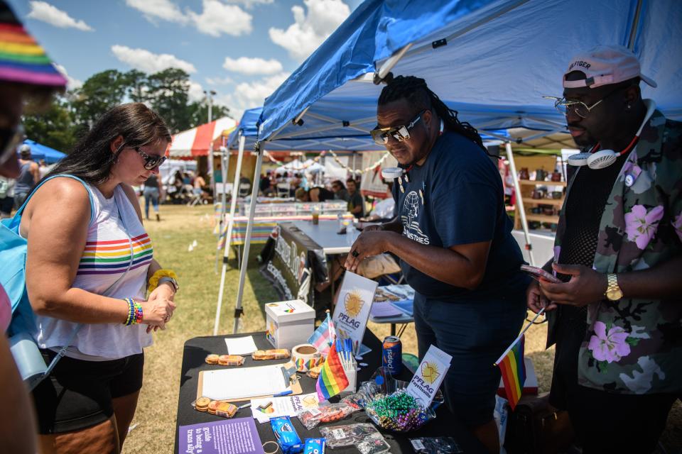 Fayetteville Chapter of PFLAG President Derrick Montgomery, center, and Vice President Aaron Brooks, right, talk with people stopping by the PFLAG booth at the Fayetteville PrideFest on Saturday, June 25, 2022, at Festival Park.