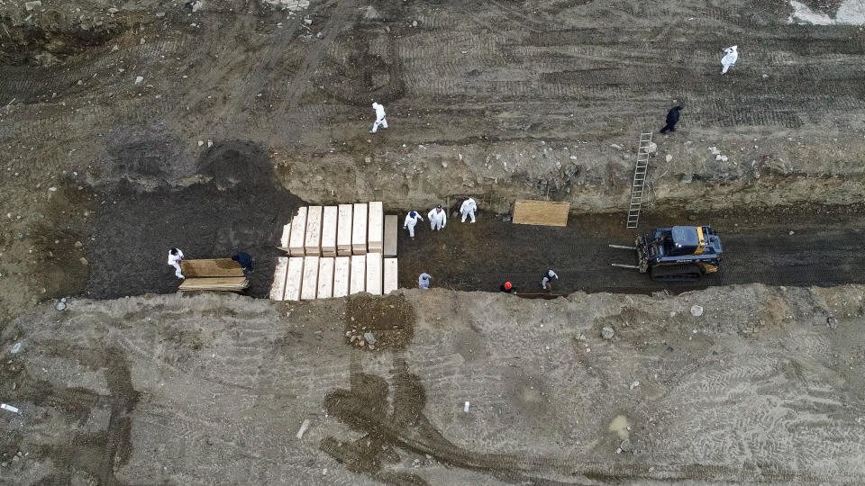 Workers wearing personal protective equipment bury bodies in a trench on Hart Island, Thursday, April 9, 2020, in the Bronx borough of New York. On Thursday, New York City’s medical examiner confirmed that the city has shortened the amount of time it will hold on to remains to 14 days from 30 days before they will be transferred for temporary internment at a City Cemetery. Earlier in the week, Mayor Bill DeBlasio said that officials have explored the possibility of temporary burials on Hart Island, a strip of land in Long Island Sound that has long served as the city’s potter’s field. (AP Photo/John Minchillo)