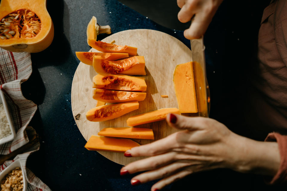 A kitchen knife cutting vegetables on a small wooden cutting board