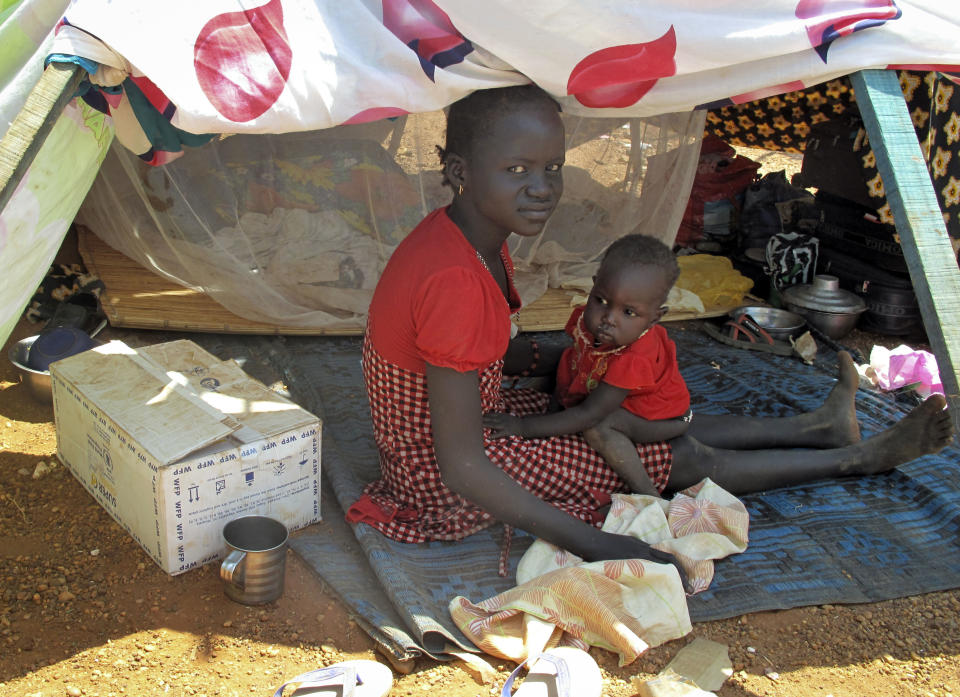 In this photo taken Monday, Dec. 23, 2013 and released by the World Food Programme (WFP), a woman and child sit in the shade next to a box of food assistance they have received in the UN compound where they have sought shelter in Juba, South Sudan.  (AP Photo/WFP, George Fominyen)
