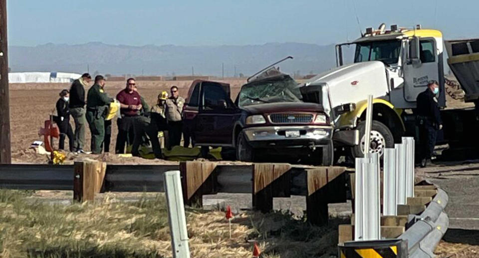 Authorities stand near a mangled SUV at the scene of a crash with a semi trailer.