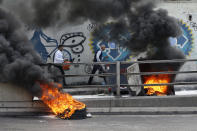 People walk next to tires set on fire by anti-government protesters to block a road during a demonstration, in Beirut, Lebanon, Sunday, Sept. 29, 2019. Hundreds of Lebanese are protesting an economic crisis that has worsened over the past two weeks, with a drop in the local currency for the first time in more than two decades. (AP Photo/Bilal Hussein)