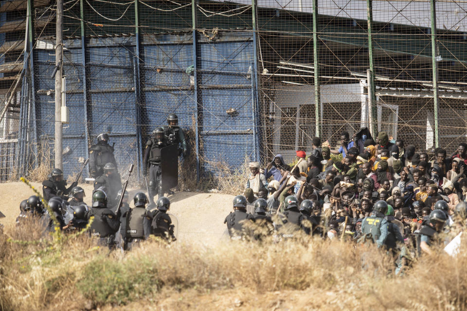 Riot police officers, left, cordon off the area after migrants arrive on Spanish soil and crossing the fences separating the Spanish enclave of Melilla from Morocco in Melilla, Spain, Friday, June 24, 2022. Dozens of migrants stormed the border crossing between Morocco and the Spanish enclave city of Melilla on Friday in what is the first such incursion since Spain and Morocco mended diplomatic relations last month. (AP Photo/Javier Bernardo)