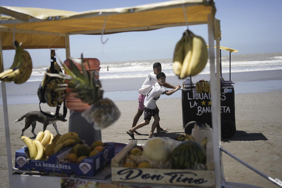 Smoothie vendors push their cart along the shore in search of customers, in Las Toninas, Argentina, Friday, Jan. 19, 2024. (AP Photo/Rodrigo Abd)