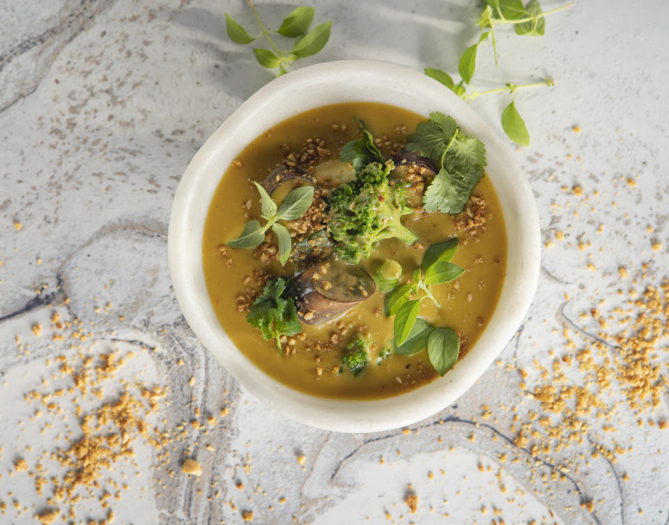 White bowl of lentils soup with broccoli over a marble countertop