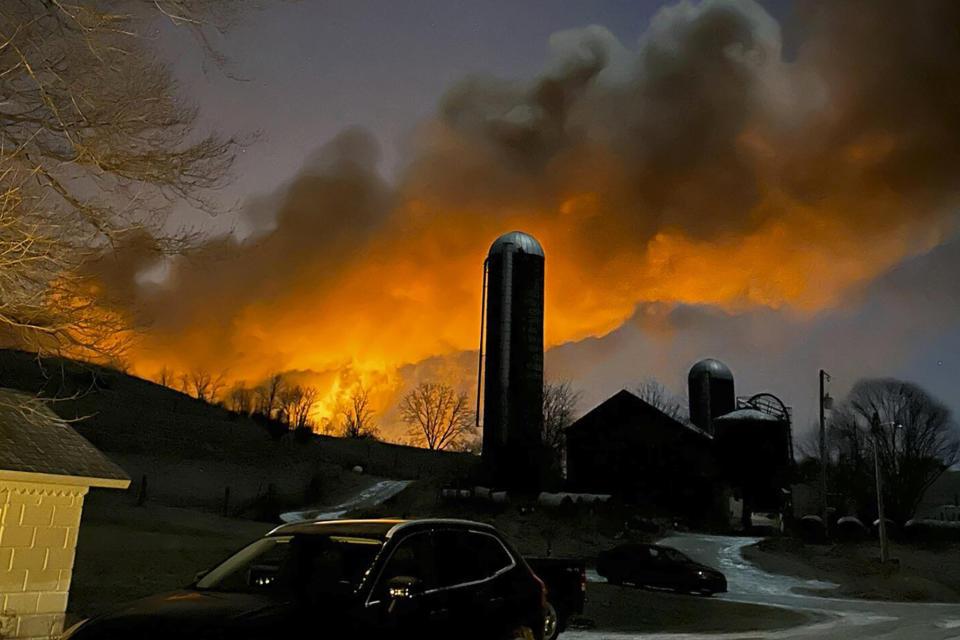 In this photo provided by Melissa Smith, a train fire is seen from her farm in East Palestine, Ohio, Friday, Feb. 3, 2023. A train derailment and resulting large fire prompted an evacuation order in the Ohio village near the Pennsylvania state line on Friday night, covering the area in billows of smoke lit orange by the flames below. (Melissa Smith via AP)