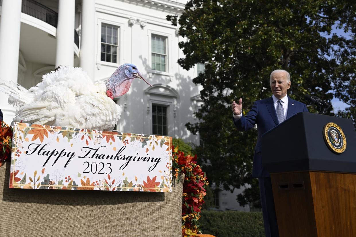 President Biden gestures toward Liberty the turkey during a pardoning ceremony on the White House grounds. A sign in front of Liberty reads: Happy Thanksgiving 2023.