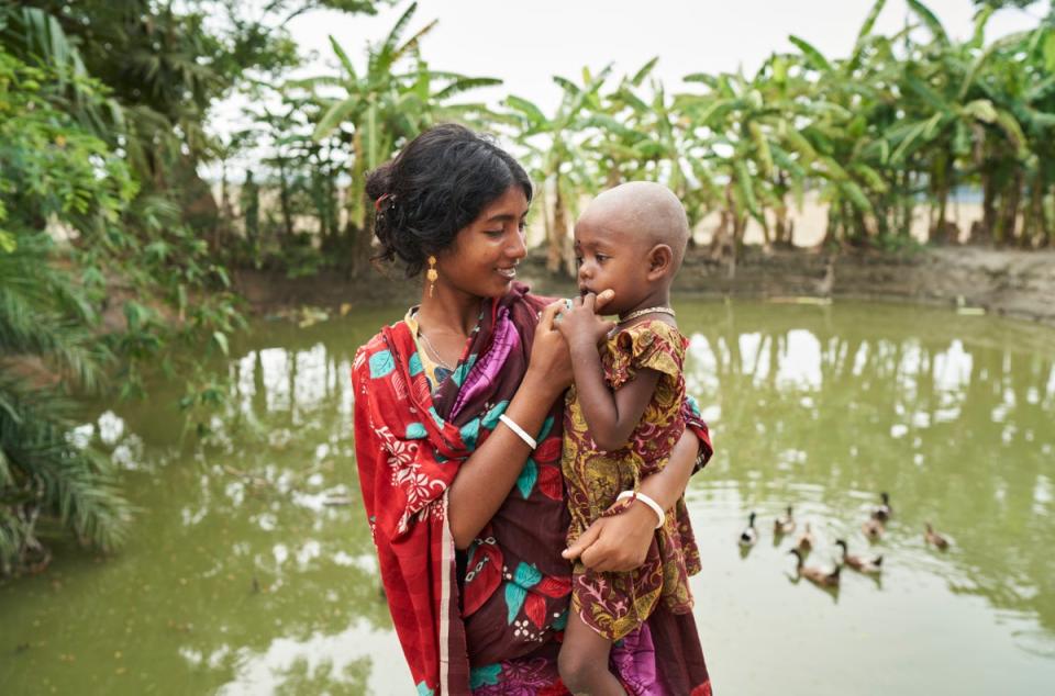 Jhorna, 22, and her daughter Obonita, 3, in front of the pond they use for washing (WaterAid/Fabeha Monir)