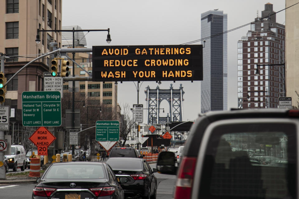 FILE - In this Thursday, March 19, 2020 file photo, The Manhattan bridge is seen in the background of a flashing sign urging commuters to avoid gatherings, reduce crowding and to wash hands in the Brooklyn borough of New York. A year after becoming a global epicenter of the coronavirus pandemic, New York and New Jersey are back atop the list of U.S. states with the highest rates of infection.(AP Photo/Wong Maye-E, File)