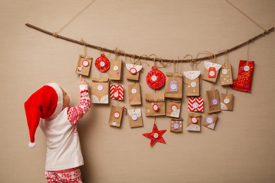 child looks at the advent calendar. Baby girl in a Christmas hat and pajamas shows on first gift.