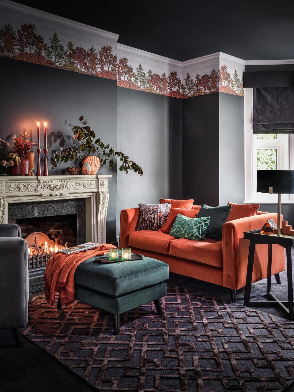 gray and orange living room with emerald green footstool, orange sofa, ornate fireplace, candles, foliage and vases on mantel, fall freeze, textured rug